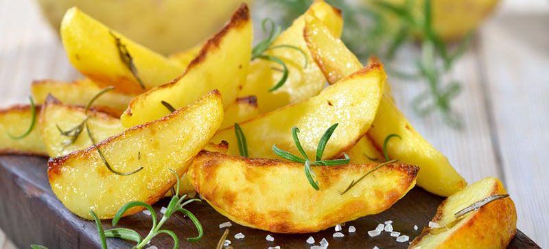 Knuspige Kartoffelspalten mit Rosmarin auf einem alten Schneidebrett
